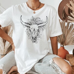 Peut inclure: T-shirt blanc avec un motif noir et blanc de cr&acirc;ne de taureau avec des d&eacute;tails floraux.
