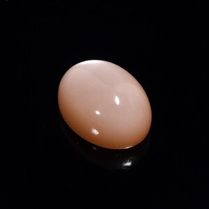 May include: A smooth, oval-shaped, light pink gemstone with a subtle shimmer.