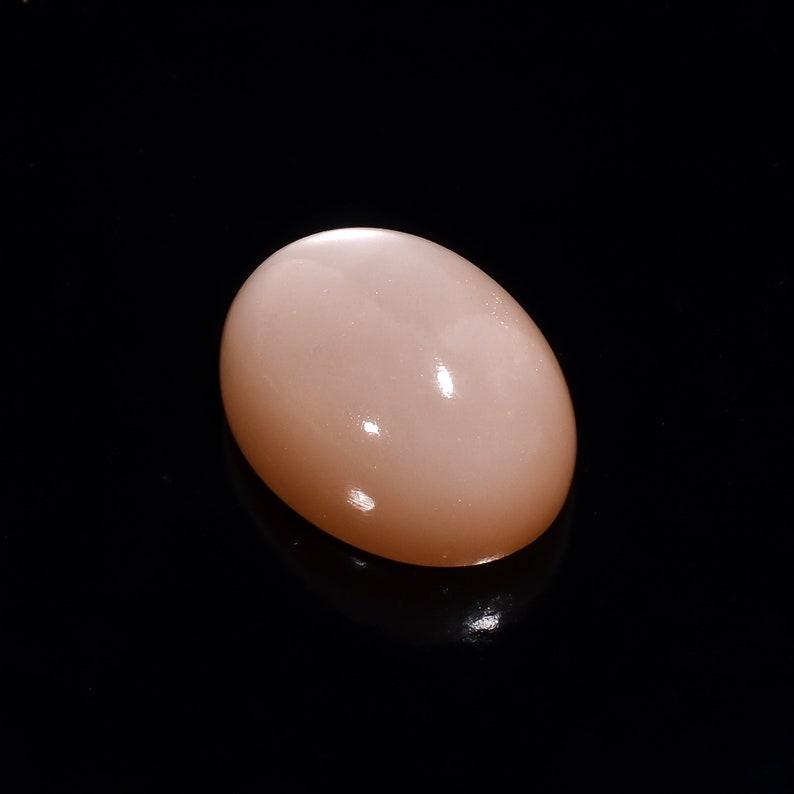 May include: A smooth, oval-shaped, light pink gemstone with a subtle shimmer.