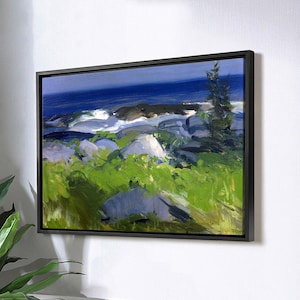 Puede incluir: Una pintura enmarcada de un paisaje marítimo con una costa rocosa, vegetación verde y un cielo azul. La pintura está colgada en una pared blanca sobre una mesa de comedor.