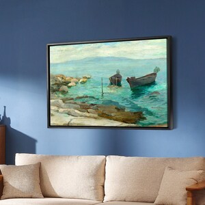May include: A beige sofa with two pillows sits in front of a blue wall with a framed painting of a seascape with two boats. A wooden coffee table with a magazine on top sits in front of the sofa.