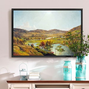 May include: A framed landscape painting of a valley with a river winding through it. The painting is hanging on a white wall above a white desk with two blue glass vases and a lantern on top of it.