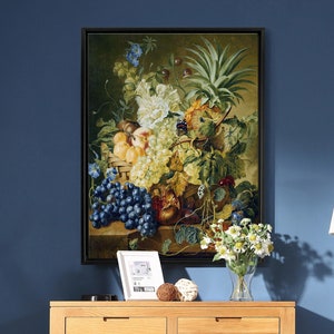 May include: A framed still life painting featuring a basket overflowing with various fruits, including grapes, peaches, and a pineapple. White and blue flowers and green foliage surround the fruit. The painting is displayed above a wooden dresser.