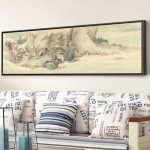 May include: A framed black and white landscape painting of a snowy mountain scene with trees and a river. The painting is hanging on a white wall above a white couch with blue and white striped cushions.