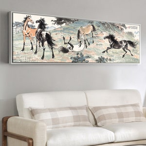 May include: A framed black and white ink painting of four horses running in a field. The painting is on a white wall above a white couch with two pillows.