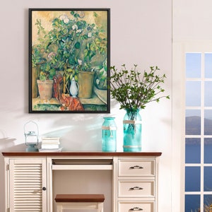 Peut inclure: Une peinture de nature morte encadrée représentant une plante en pot, un vase et un pichet. La peinture est dans un cadre en bois clair et est accrochée à un mur blanc. La peinture est de style vintage et présente des couleurs douces.