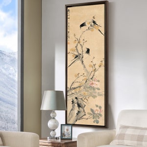 May include: A framed painting of two black and white birds perched on a branch of a flowering tree. The tree has yellow flowers and pink blossoms. The painting is on a beige background with black calligraphy in the upper left corner.
