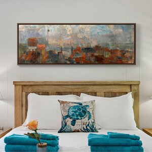 May include: A framed painting of a cityscape with a hazy sky. The painting is in a brown frame and is hanging on a white wall above a wooden headboard. The headboard is decorated with a white pillow with a blue sea turtle design.