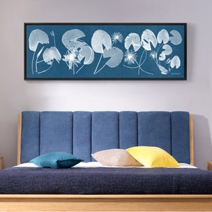 May include: A blue headboard with a light blue and white floral print framed artwork above it. The headboard is made of fabric and has a tufted design. The artwork is a long rectangular print with a white frame.