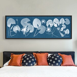 May include: A framed print of a blue background with white silhouettes of water lily leaves and flowers.