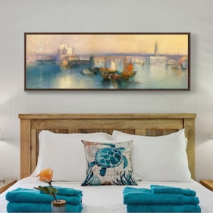 May include: A framed painting of a seascape with boats and a city in the background. The painting is hanging above a bed with white bedding and blue towels.