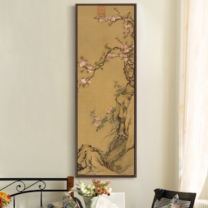 May include: A framed painting of a delicate branch of pink blossoms with birds perched on the branches. The painting is set against a light brown background and features a rocky cliff face.