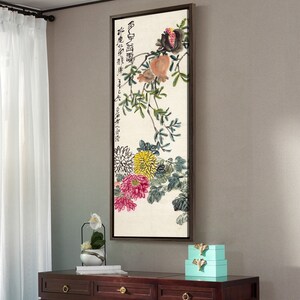 May include: A framed painting of a floral arrangement with a pomegranate branch. The painting is in a brown frame and features a white background with a branch of green leaves, pink and yellow flowers, and a pomegranate with red and orange fruit. The painting has Chinese characters in black ink.