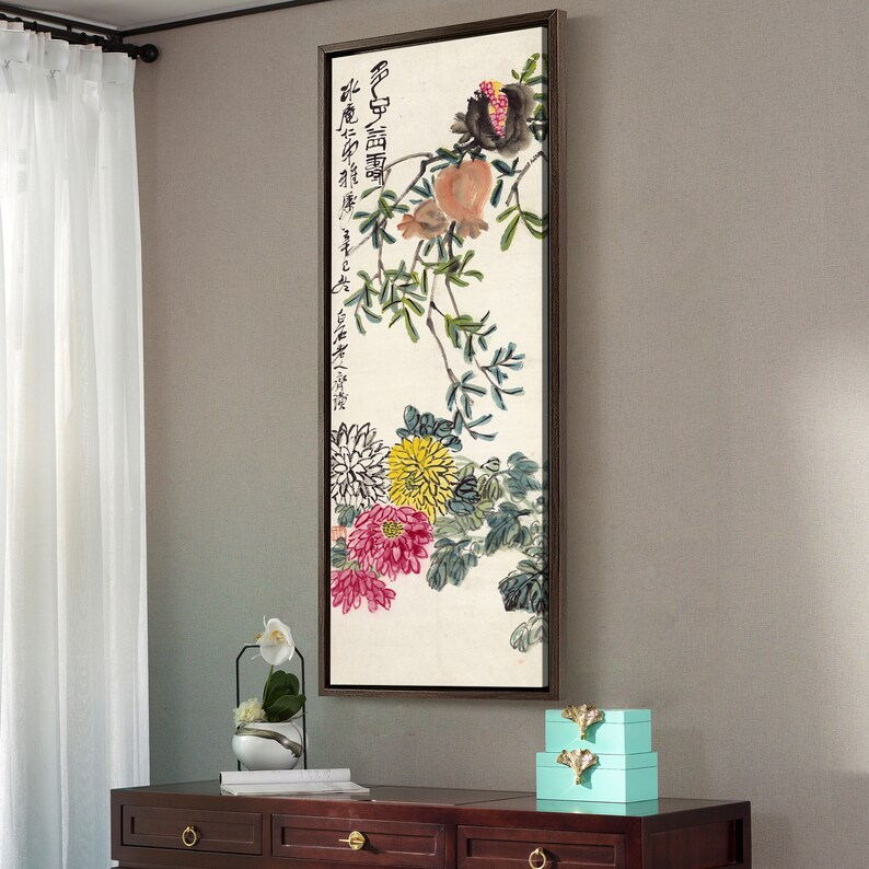 May include: A framed painting of a floral arrangement with a pomegranate branch. The painting is in a brown frame and features a white background with a branch of green leaves, pink and yellow flowers, and a pomegranate with red and orange fruit. The painting has Chinese characters in black ink.