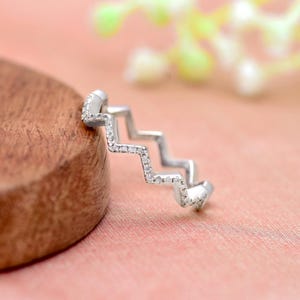 Könnte beinhalten: Ein silberner Ring mit einem Zickzack-Design, besetzt mit kleinen Diamanten.