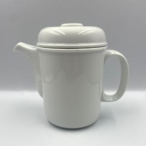 Puede incluir: Tetera de cerámica blanca con tapa y asa. La tetera tiene un diseño sencillo y es perfecta para preparar té.