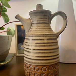 May include: A brown and white ceramic pitcher with a striped design and a decorative base. The pitcher has a spout and a handle.