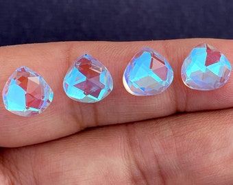 Puede incluir: Cuatro piedras preciosas iridiscentes en forma de pera con un tono azul claro y rosa.