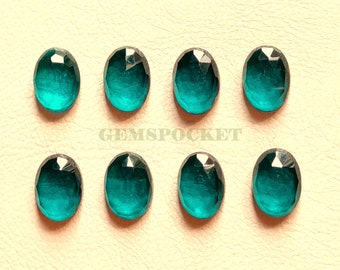May include: Eight oval-shaped teal green gemstones with faceted edges. The gemstones are arranged in two rows of four on a light beige surface. The text "GEMSPOCKET" is printed in black below the gemstones.