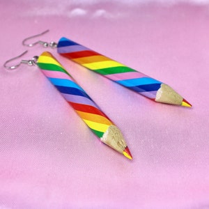 Könnte beinhalten: Ein Paar Regenbogen-Bleistift-Ohrringe. Die Ohrringe sind aus Holz und haben einen silbernen Haken.