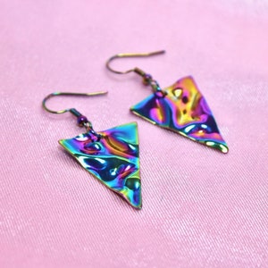 May include: A pair of iridescent triangle earrings with a wavy, textured surface. The earrings are made of metal and have a silver hook.