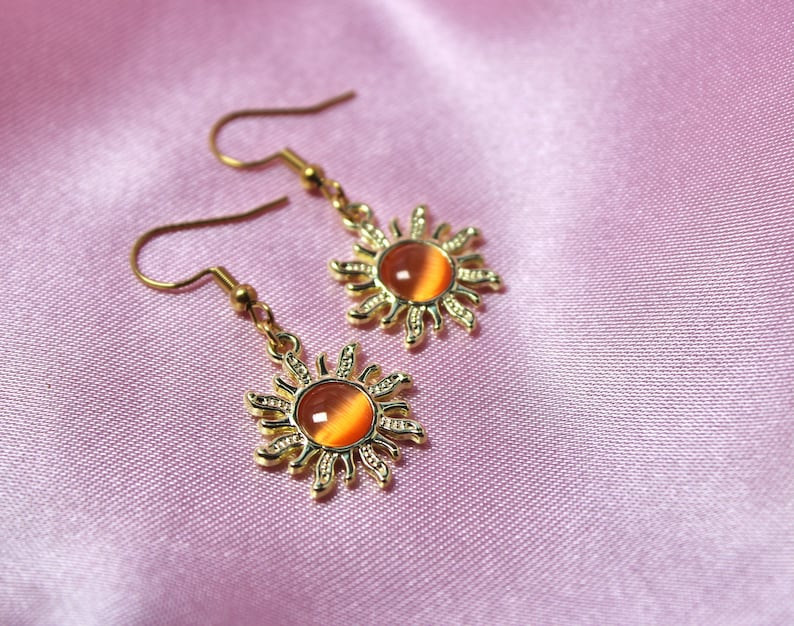 May include: A pair of gold earrings with a sun design and orange gemstone accents.