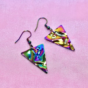 May include: A pair of iridescent triangle earrings with a textured surface. The earrings are made of metal and have a silver hook.