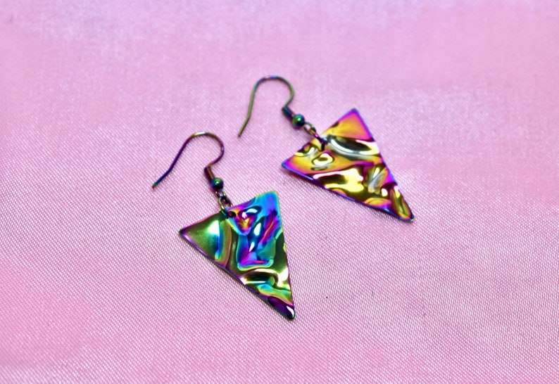 May include: A pair of iridescent triangle earrings with a textured surface. The earrings are made of metal and have a silver hook.