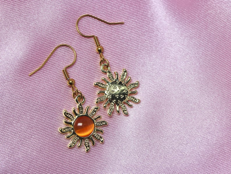 May include: A pair of gold sun earrings with orange glass stones. The earrings have a delicate, intricate design.
