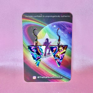 May include: A pair of iridescent triangle earrings with a holographic finish. The earrings are on a card with a rainbow background and the text "be bold, confident & unapologetically authentic." and "@TheRainbowRockstar".