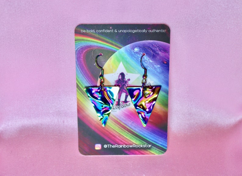 May include: A pair of iridescent triangle earrings with a holographic finish. The earrings are on a card with a rainbow background and the text "be bold, confident & unapologetically authentic." and "@TheRainbowRockstar".