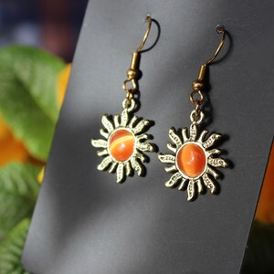 May include: A pair of gold sun earrings with orange and yellow gemstone accents.