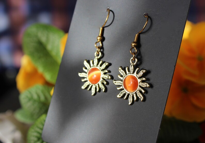 May include: A pair of gold sun earrings with orange and yellow gemstone accents.