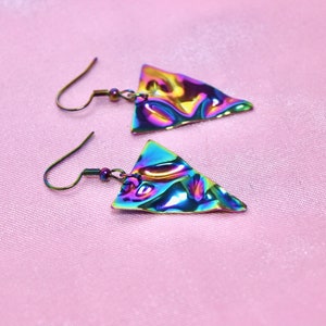 May include: A pair of iridescent triangle earrings with a textured surface. The earrings are made of metal and have a silver hook.