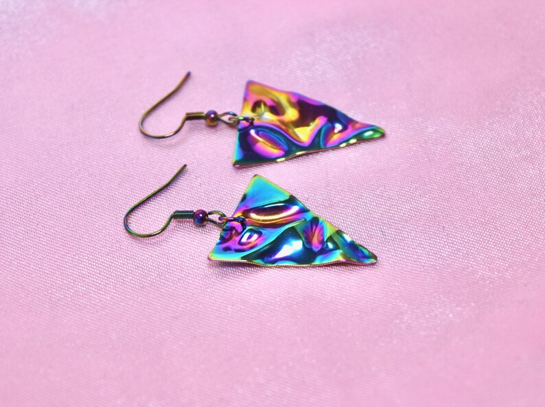 May include: A pair of iridescent triangle earrings with a textured surface. The earrings are made of metal and have a silver hook.