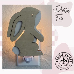 May include: A wooden bunny night light with a light tan body and white accents. The bunny is plugged into a white outlet. The words "Digital File" are written in cursive. The logo for Pacific Saints is in the bottom right corner.
