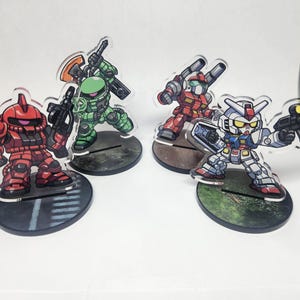 May include: Four colorful acrylic Gundam robot figures, each mounted on a circular base. The robots are red, green, red-orange, and white with blue and red accents. Each figure is holding a weapon, and the bases have different designs.