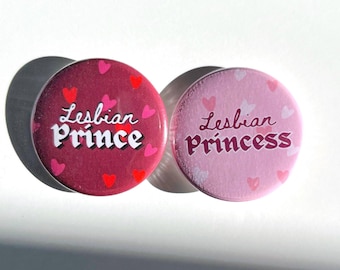 May include: Two round pink and red buttons with white text. The pink button says "Lesbian Princess" and the red button says "Lesbian Prince". Both buttons have small pink and red hearts scattered around the text.