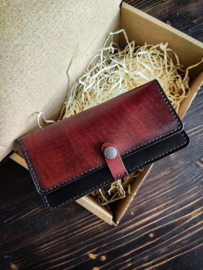May include: A black and burgundy leather wallet with a silver button closure. The wallet is personalized with the name "Sonja".