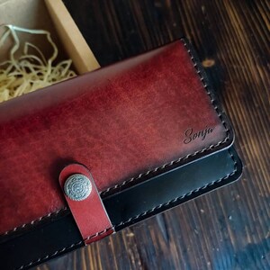 May include: A burgundy leather wallet with a black leather trim and a silver snap closure. The wallet has the name "Sonja" embossed on the front.