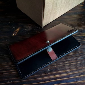 May include: A black and brown leather wallet with a silver button closure. The wallet has the word "Samir" embossed on the front.
