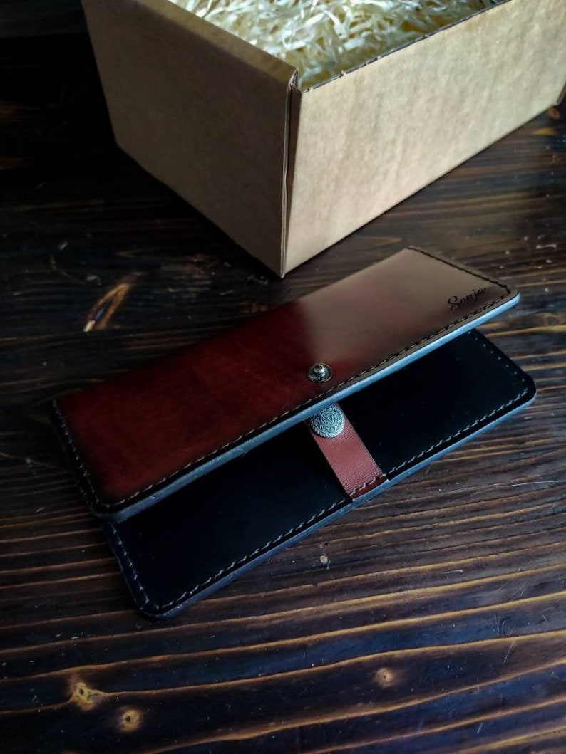 May include: A black and brown leather wallet with a silver button closure. The wallet has the word "Samir" embossed on the front.