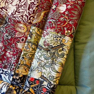 May include: A patchwork fabric with a floral pattern in shades of red, green, and gold. The fabric is folded over itself, revealing the different patterns. The fabric is on a green background.