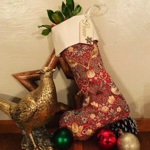 May include: A Christmas stocking with a red floral pattern, a white cuff, and a wooden tag that says "Peace". A gold pheasant statue and Christmas ornaments are in the foreground.