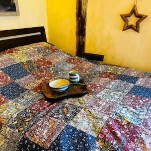 May include: A bed with a patchwork quilt featuring a floral and bird pattern. A wooden tray with a bowl and two mugs sits on the quilt.
