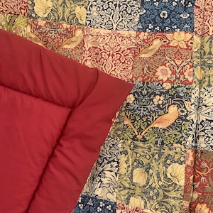 May include: A red quilt with a patchwork design featuring various floral patterns in shades of green, blue, and brown. The quilt is made of cotton fabric and has a soft, comfortable feel.
