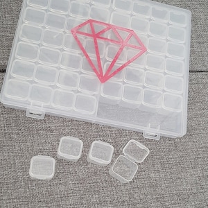 Könnte beinhalten: Eine transparente Plastik-Aufbewahrungsbox mit 48 kleinen Fächern. Die Box hat eine Diamantform auf dem Deckel. Es gibt sechs kleine Fächer außerhalb der Box.