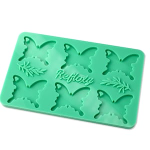 Könnte beinhalten: Grüne Silikonform mit sechs Schmetterlingsformen und zwei Zweigen mit Blättern. Die Form ist mit "Refloxy" beschriftet.