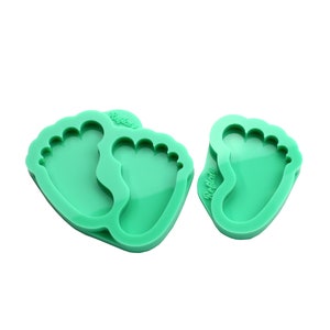 May include: Two green silicone moulds shaped like baby footprints. The moulds are designed for making resin crafts.