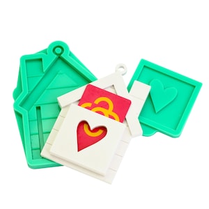 Könnte beinhalten: Eine Sammlung von Bastelformen in Haus- und Quadratform. Die Formen sind grün und weiß, mit Herz- und abstrakten Designs. Die Hausform hat ein Dach und ein Loch zum Aufhängen. Die quadratische Form hat eine Herzform.